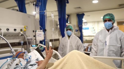 karachi , Pakistan - 02 15 2021: Elderly Covid ICU Patient Waving Holding Up Mobile Phone In Hospital. Slow Motion, Follow Shot
