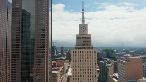 Aerial view of tall building with spike and large clock. Pedestal up footage following Mercantile National Bank. Downtown skyscrapers. Dallas, Texas, US