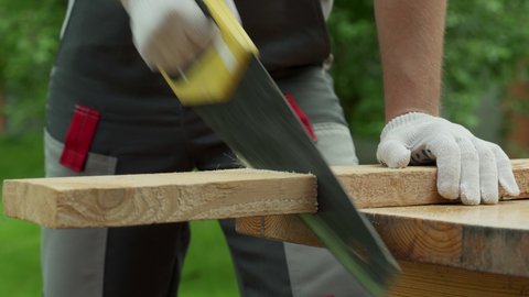 Man carpenter saws a wooden board with a hand saw. 
