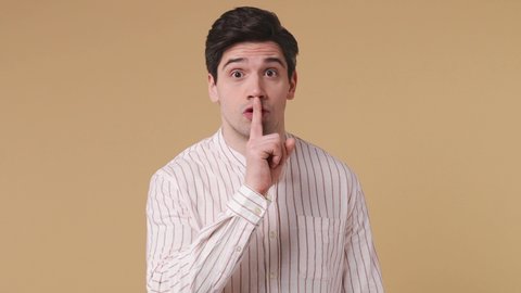 Secret young man 20s years old wear white striped shirt look aside say hush be quiet with finger on lips shhh gesture close her mouth lock and throw away key isolated on pastel beige background studio