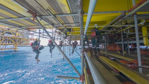 4K time lapse of scaffold erector team with falling protection hanging on scaffold frames below oil and gas platform during working overboard in the middle of the sea.