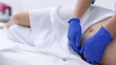 Close up of female gynecologist in medical gloves performing palpation of pregnant woman. Physiotherapist woman massaging tummy on pregnant woman on a stretcher.