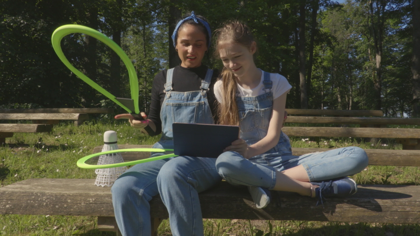 Woman with her daughter using digital tablet for learning badminton game
