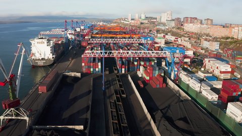 Vladivostok, Russia - May 11, 2021: Aerial drone footage of a cargo terminal with ships. The terminal operates gantry cranes. The containers are stacked. Railway wagons with coal
