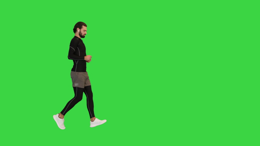 Running athlete man looking at smartwatch heart rate and listening to music in earphones on a Green Screen, Chroma Key.