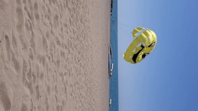 Yellow parachute for parasailing recreational activity. Unrecognizable man jogging by waters edge at sea. Vertical format video textile parasail wing flying in wind on beach sand at sea shore