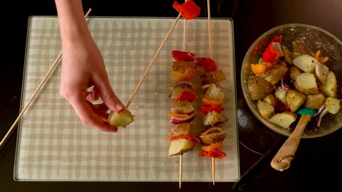 4K top down view of woman making vegetable kabobs to grill with potatoes, peppers and onions. Woman's hand threading food onto skewer. Series.