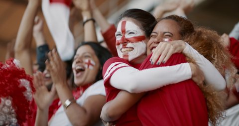 Female soccer fans of England watching and starts celebrating after their team's victory. English female spectators enjoying after a win at stadium.

