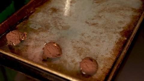 4K clip of woman's hand placing double chocolate cookie dough balls onto an old, rustic cookie sheet using a cookie baller. Baking, series.