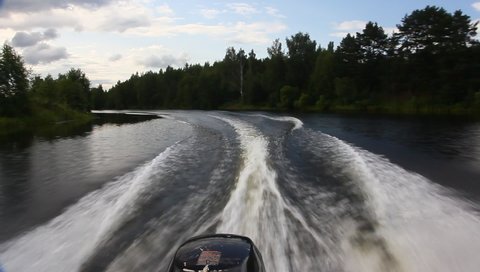 Powerboat turns on the river water with circle keelwater trail on dark banks background at summer day, POV back view on foamy transom wake from stern of motor boat with single outboard motor