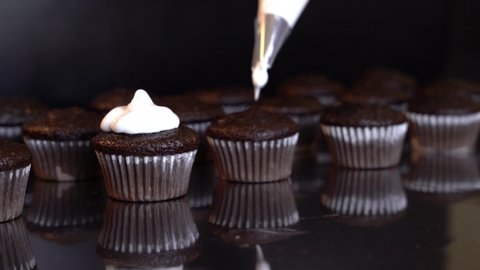 4K clip of icing mini smores cupcakes with a piping bag on a black background, cupcake reflections can be seen. Baking, series. 