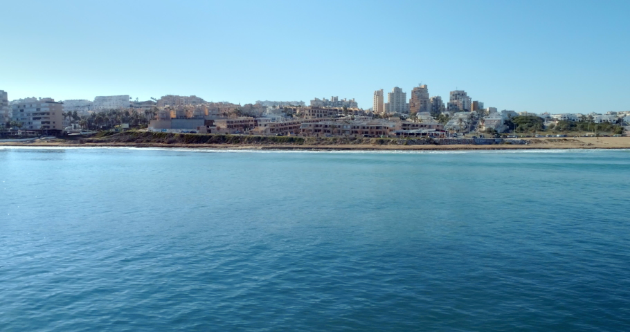 Drone fly above sea along the coastline rocks and looking to the cityscape