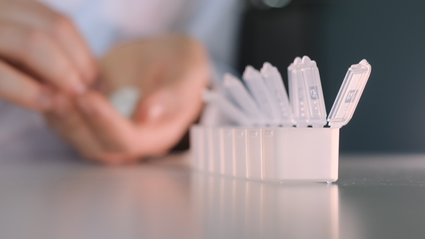 hand female doctor lays out put white pills in container. Organizer for drugs in which the patient puts tablets. Rack focus.