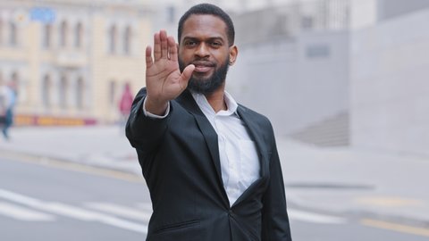 Serious strong decisive African bearded young adult ethnic male puts palm in front of him, confidently shows stop gesture, against violence, demonstrate NO sign, distance, defends personal boundaries