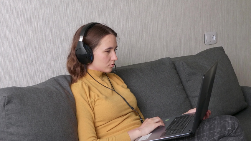 young woman is completing work on a laptop. A girl looks at the screen, closes the laptop and removes headphones. Remote work freelancer at home workplace.