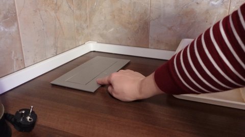 Person in red striped pullover presses button and grey black designed outlets appear on wooden table edge in hotel room closeup