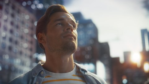 Portrait of a Happy Handsome Young Man in Casual Clothes Standing on the Street at Sunset. Stylish Male Model in Big City Living the Urban Lifestyle. Background with Office Buildings and Billboards.