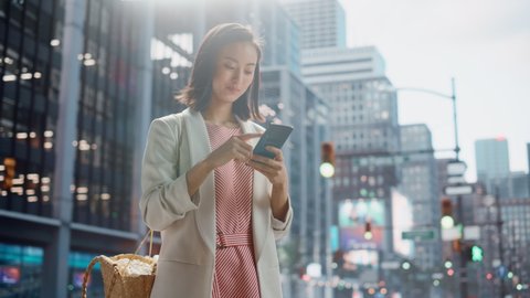 Portrait of a Beautiful Japanese Female Wearing Smart Casual Clothes and Using Smartphone on the Urban Street. Manager in Big City Connecting with People Online, Messaging and Browsing Internet.
