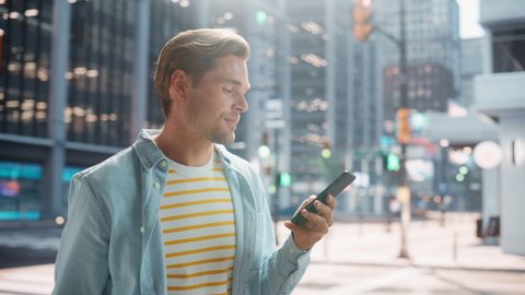 Portrait of a Handsome Young Man Walking in Casual Clothes and Using Smartphone on the Urban Street. Smiling Male in Big City Connecting with People Online, Messaging and Browsing Internet.