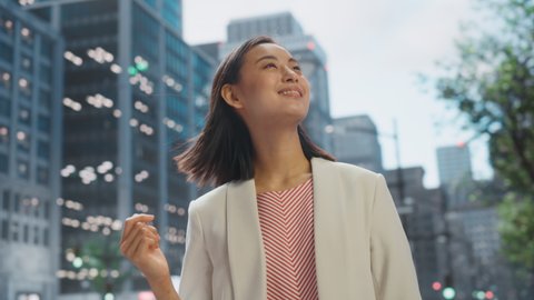 Portrait of Beautiful Japanese Female Wearing Smart Casual Clothes Posing on the Street. Successful Female in Big City Living the Urban Lifestyle. Background with Office Buildings and Billboards.