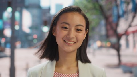 Portrait of Beautiful Japanese Female Wearing Smart Casual Clothes Posing on the Street. Successful Female in Big City Living the Urban Lifestyle. Background with Office Buildings and Billboards.