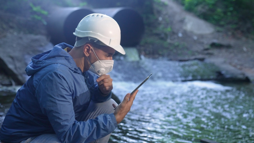 water treatment engineer examines environmental pollution. biologist with digital tablet examines water allergy. worker in a helmet works about environmental pollution. biologist sewage test water app Royalty-Free Stock Footage #1074843917