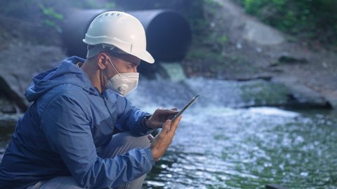 water treatment engineer examines environmental pollution. biologist with digital tablet examines water allergy. worker in a helmet works about environmental pollution. biologist sewage test water app