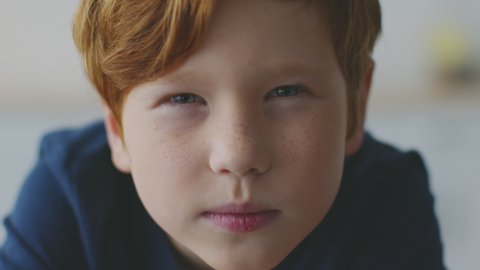 Kids eyesight problems. Close up portrait of little redhead boy with freckles squinting his eyes, peering to camera, feeling troubles with vision, reading difficulties concept, slow motion