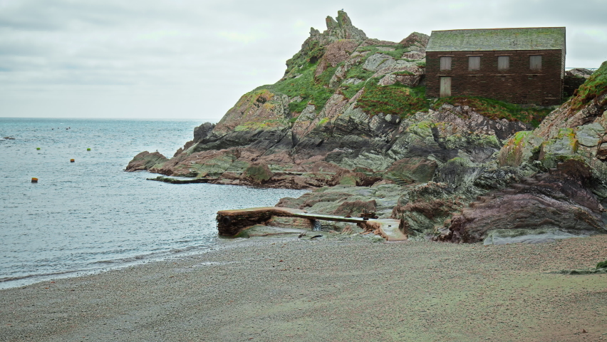 Coastline holiday houses on the rocks of a mountainous area with a view of the ocean and seagulls flying over. A 4K view to Polperro Harbour and Beach with Chapel Pool, Cornwall, England, UK.  