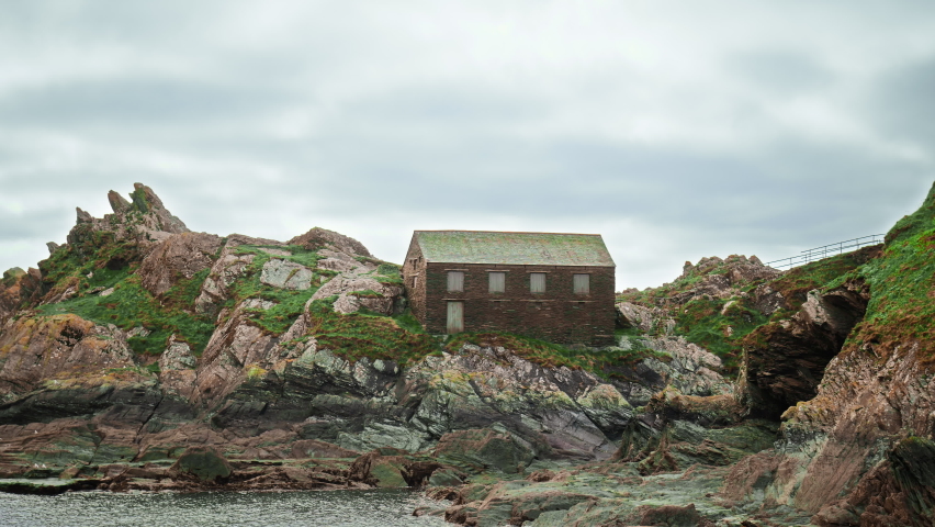 Coastline holiday houses on the rocks of a mountainous area with a view of the ocean and seagulls flying over. A 4K view to Polperro Harbour and Beach with Chapel Pool, Cornwall, England, UK.  