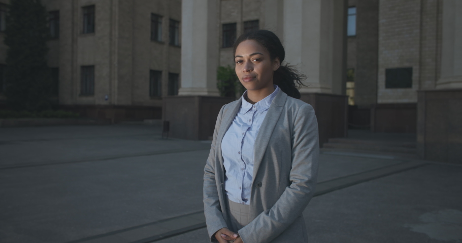 Successful career concept. Zoom in portrait of positive young african american business lady posing with crossed arms against office building, slow motion