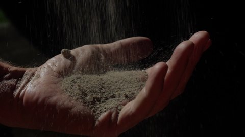 Sand falling into the hand of a male. Black background. Slow-motion 180 fps. The four elements.