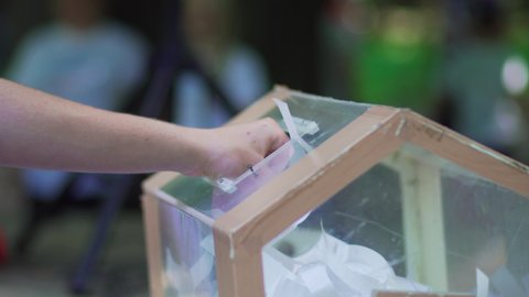 The self-made box from transparent plastic is glued in form of drum for hoax. People adult and children throw white sheets of paper with lottery numbers through open hole. Prize draw. Drum for raffle