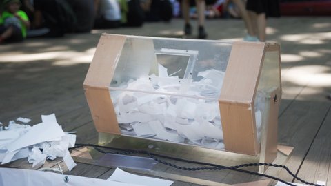 The self-made box from transparent plastic is glued in form of drum for hoax. People throw white sheets of paper with lottery numbers through open hole. Prize draw. Drum for raffle on stage