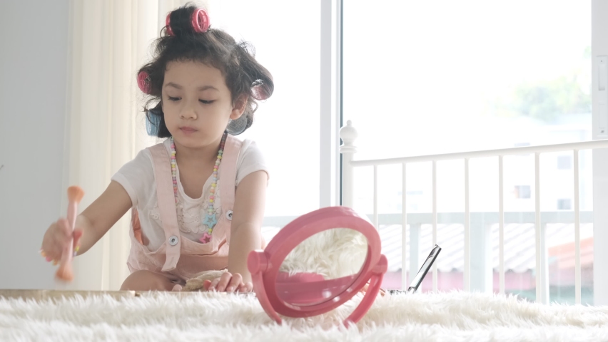 Llittle asian girl using brush make up her face on bed.
