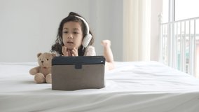 Little asian girl with headphones and looking cartoon movie with tablet on bed.education and technology concept.