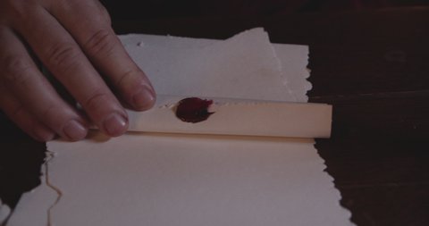 A close-up shot of a person's hands wearing a luxuriant ring with a red stone sealing a scroll made out of an old parchment paper with a red wax putting pressure on the bronze-colored stamp