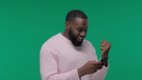 young black man excited and celebrating while holding and looking at his phone on Green Screen, Chroma Key
