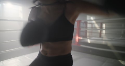 Woman Training Boxing in Boxing Ring. Female Fighter Throws Punches and Looking at Camera at Dark Ring. Portrait of Woman Kickboxer. Boxing Concept.