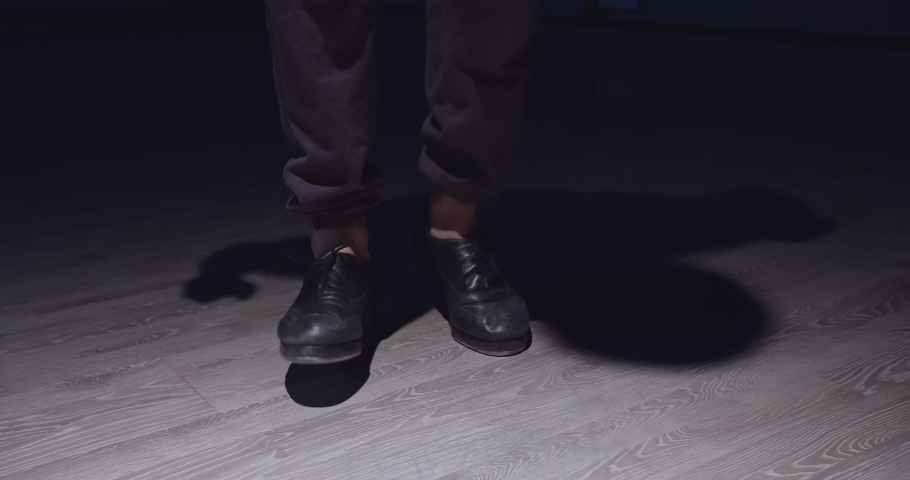 A man in black shoes is dancing a tap dance. His trousers are tucked up so you can see his bare ankles. He quickly kicks off the floor and moves them. A black shadow is visible on the floor Royalty-Free Stock Footage #1074859070