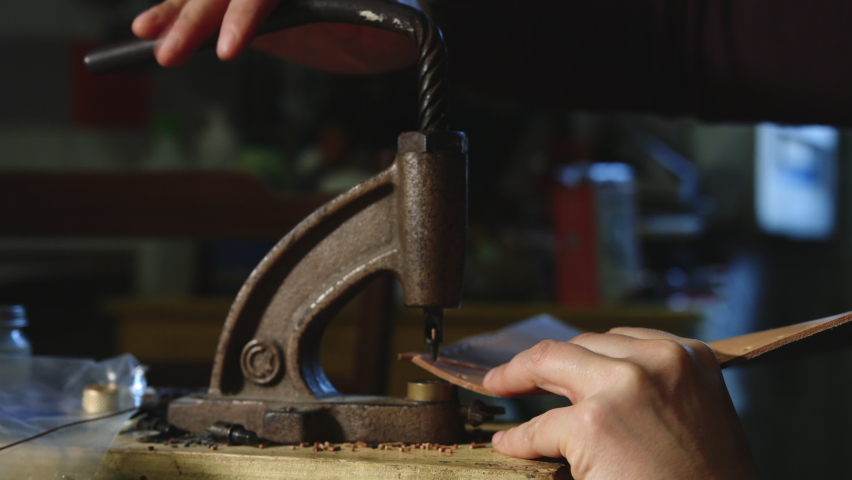 Leather craftsman at work using a hand rivet press in order to puncture leather