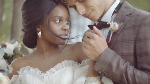 Close-up portrait of bride and groom of different races. Newlyweds hold hands at a multi-ethnic wedding