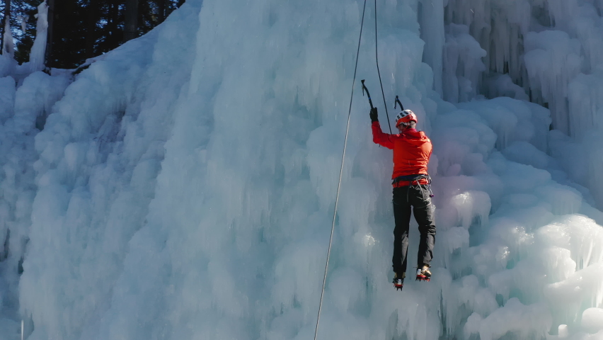 Aerial view of a frozen waterfall and rocks with climber ascending its ice-covered surface, using ice axes and crampons Royalty-Free Stock Footage #1074869003