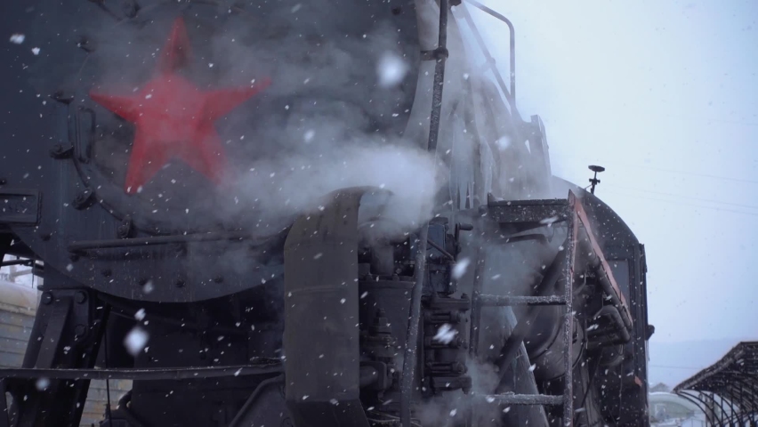 Gimbal film close-up front steel old steam locomotive historic train engine standing at railway station release white clouds. Winter frozen loco. Siberia Transsib Circum-Baikal. Travel Russia. Sunny