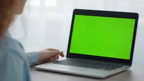 Digital education and communication. Unrecognizable little girl watching videos online on laptop with green chroma key screen, sitting at home, free space for mockup