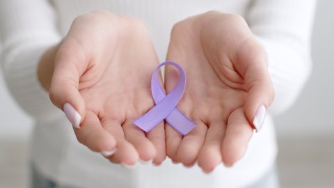 Domestic violence awareness symbol. Close up shot of female hands hands holding purple ribbon, expressing love and unity, slow motion