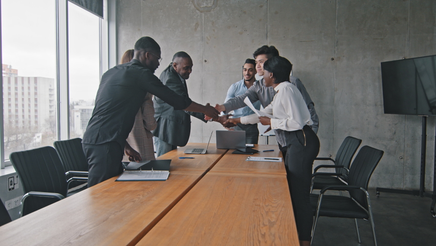 Multiracial group of colleagues multiethnic corporate workers shaking hands making handshake greeting gesture meeting in office conference sitting down at table listening report of hispanic boss man Royalty-Free Stock Footage #1074879323