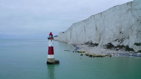 A circling aerial shot around Beachy Head lighthouse in East Sussex with the tall white chalk cliffs near Eastbourne.