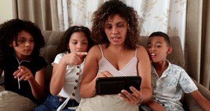 Brazilian mother and children staring at cellphone screen together at home sofa surprised reaction.