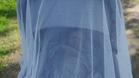 Cute caucasian baby in the baby carriage, face of 3 month old baby boy in carrycot covered with insect net closeup. High quality 4k footage